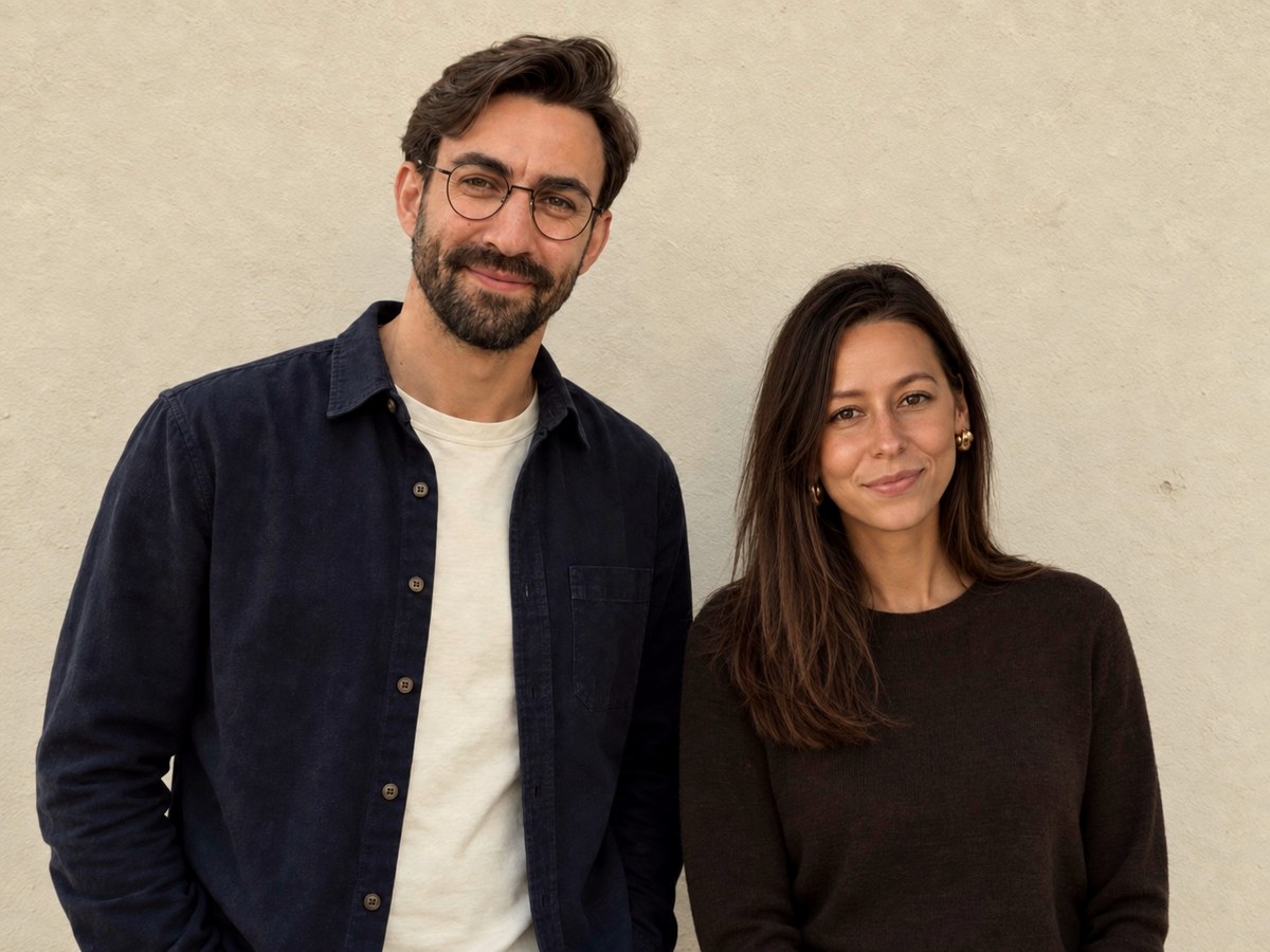 Matt and Laura, the makers of Yoke, standing side by side against a pale wall.
